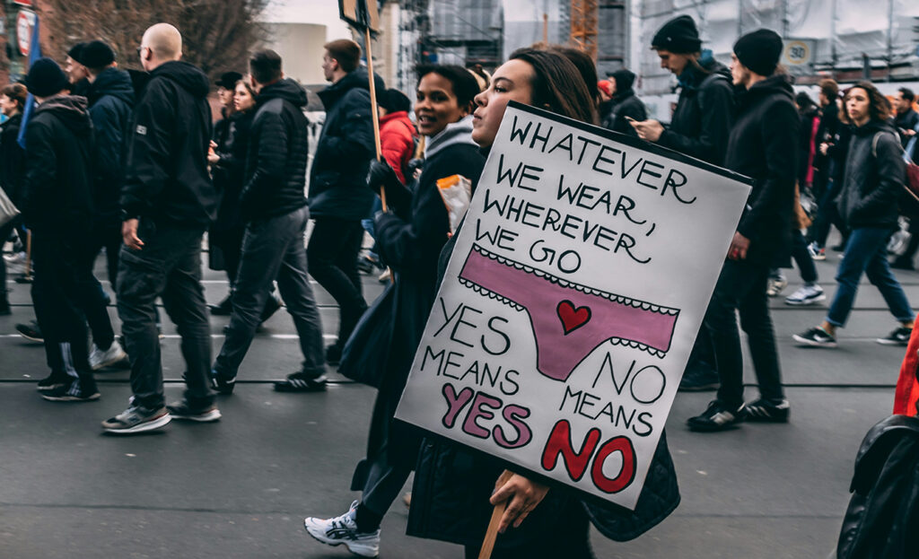 woman holding sign that reads: whatever we wear, wherever we go, yes means yes, no means no