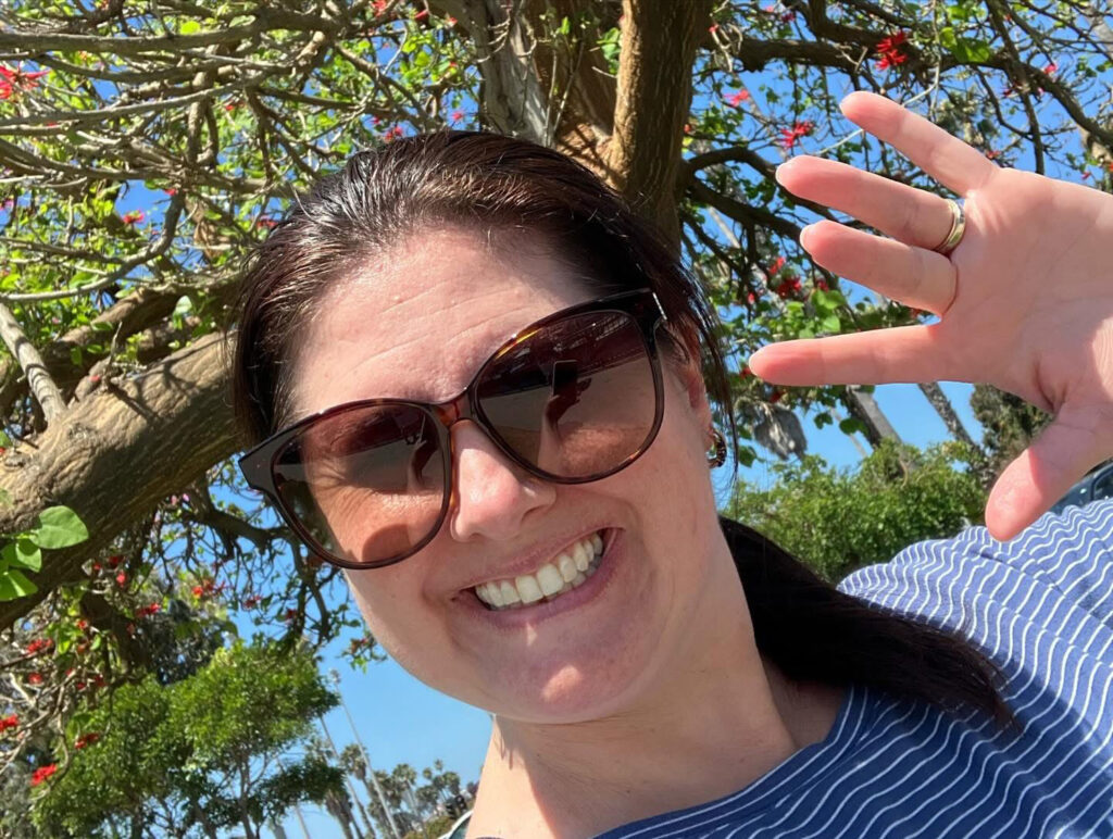 MaryLou Banuelos selfie, wearing sunglasses, waving to camera
