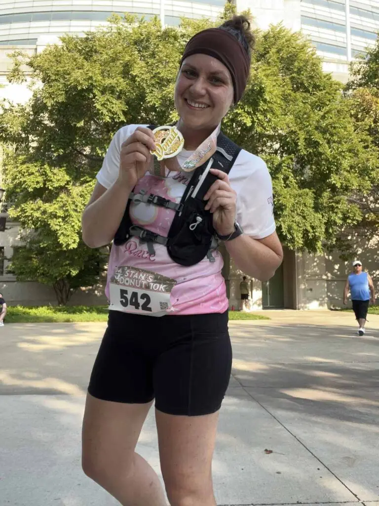 Amanda Schoenbeck finishing a race, holding her medal, smiling toward the camera