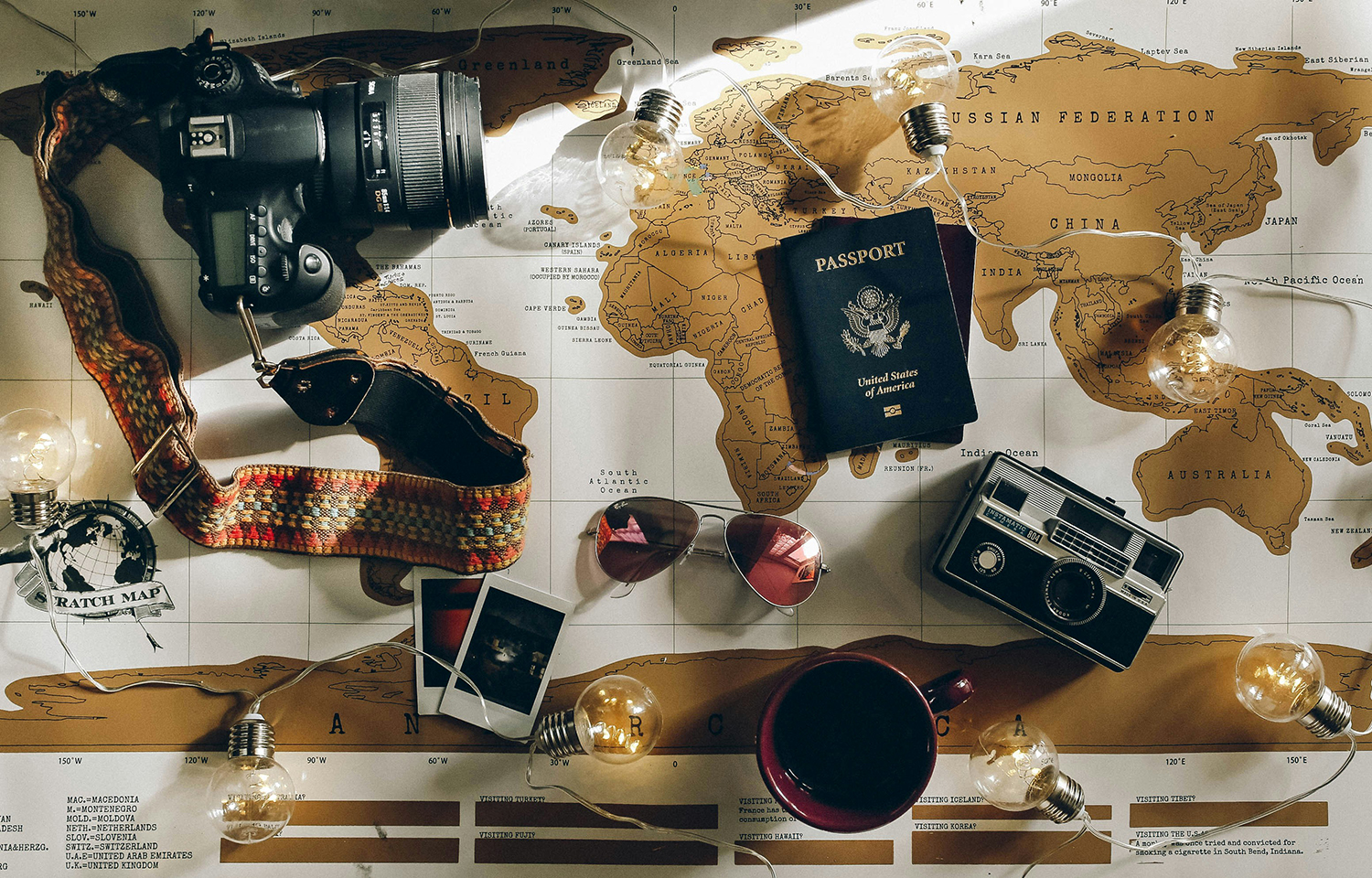 aerial view of travel accessories, including passport, camera, and sunglasses, on top of a world scratch map.